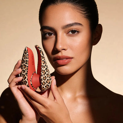 A close-up lifestyle shot of a model holding a leopard-print travel vibe in its against a warm beige background.