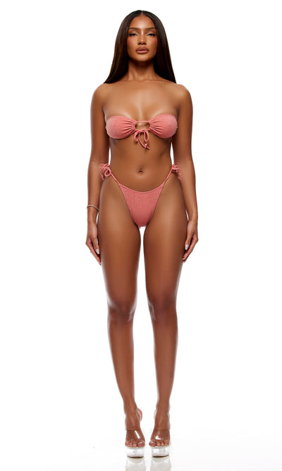 A model wearing a dusty rose pink two-piece bikini with a bandeau top and matching side-tie bottoms, standing against a solid white background.