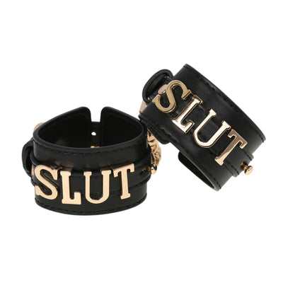 Black leather cuffs with gold 'SLUT' lettering on a white background