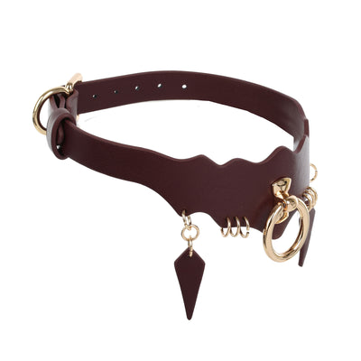 A wine-colored faux leather collar with gold-tone hardware, featuring a wavy cutout design, a dangling pointed leather tag, and a coiled spring detail, shown on a plain white background.