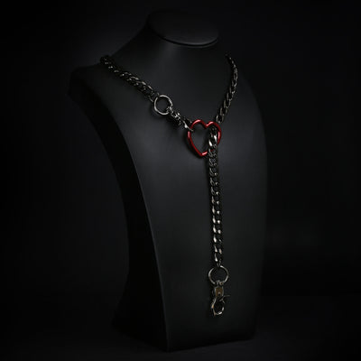A gothic-style metal collar necklace with a red heart accent and silver-toned chain, displayed on a black mannequin bust against a dark background.