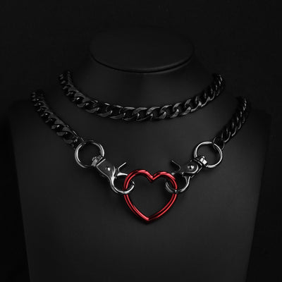 A black metal chain choker necklace displayed on a black mannequin bust, featuring a red heart-shaped ring pendant connected by silver-toned clasp hardware.