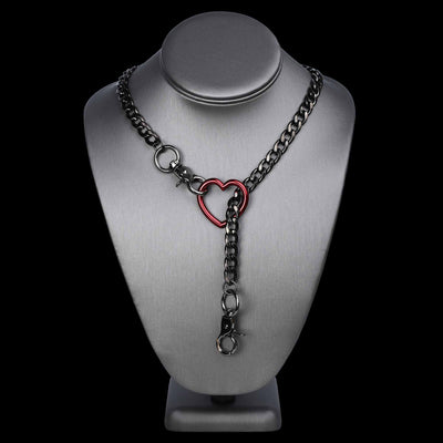A dark gunmetal chain necklace with a central red heart-shaped clasp, displayed on a silver metal jewelry bust against a solid black background.