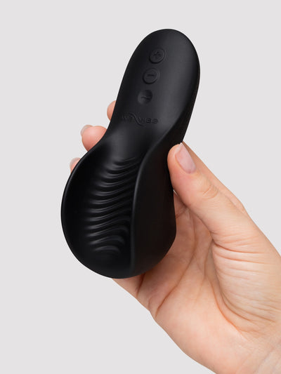 A hand holding a matte black personal massager against a light gray background.