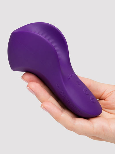 A purple personal massager held in a person's hand against a light gray background.